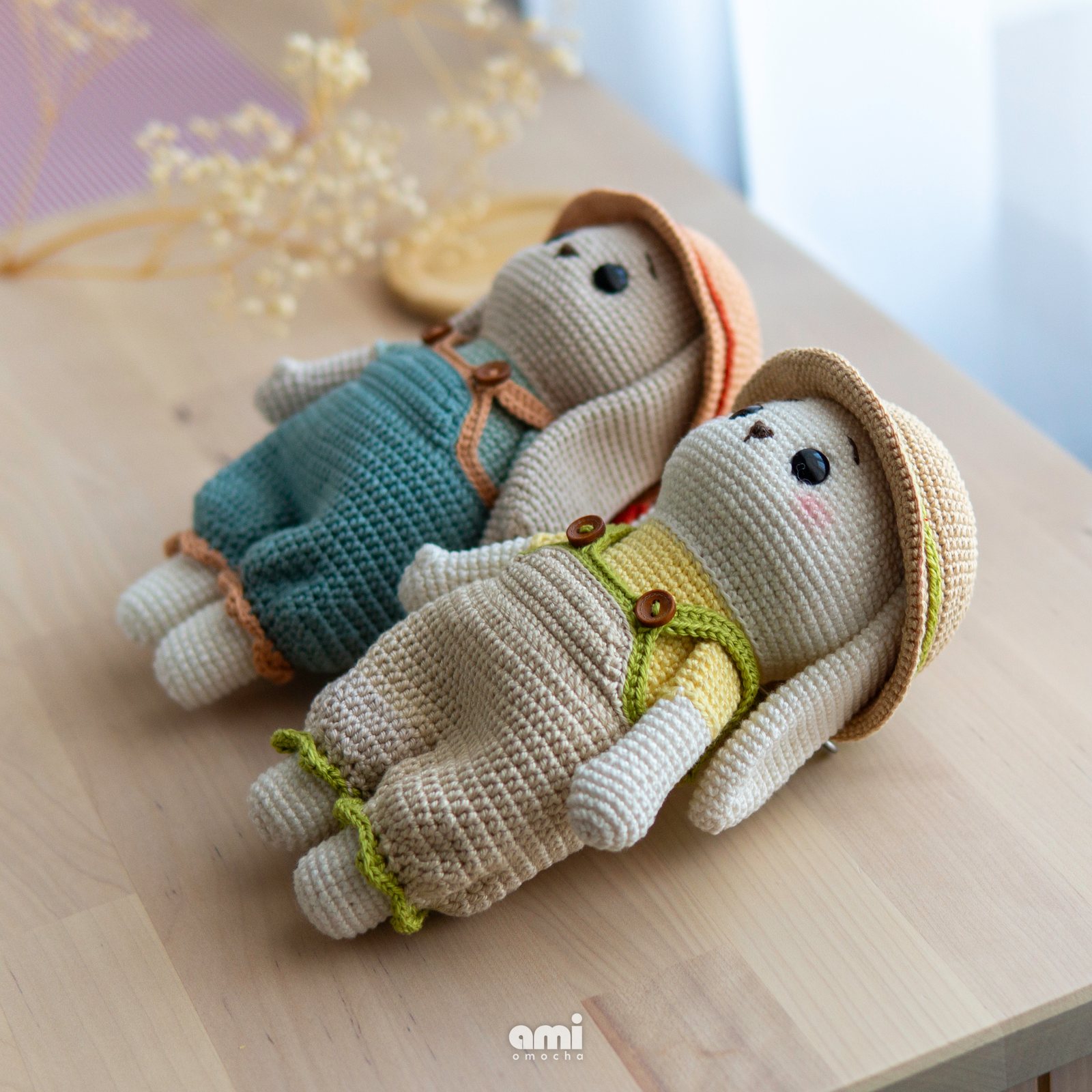 Two crocheted amigurumi bunnies in overalls and sun hats